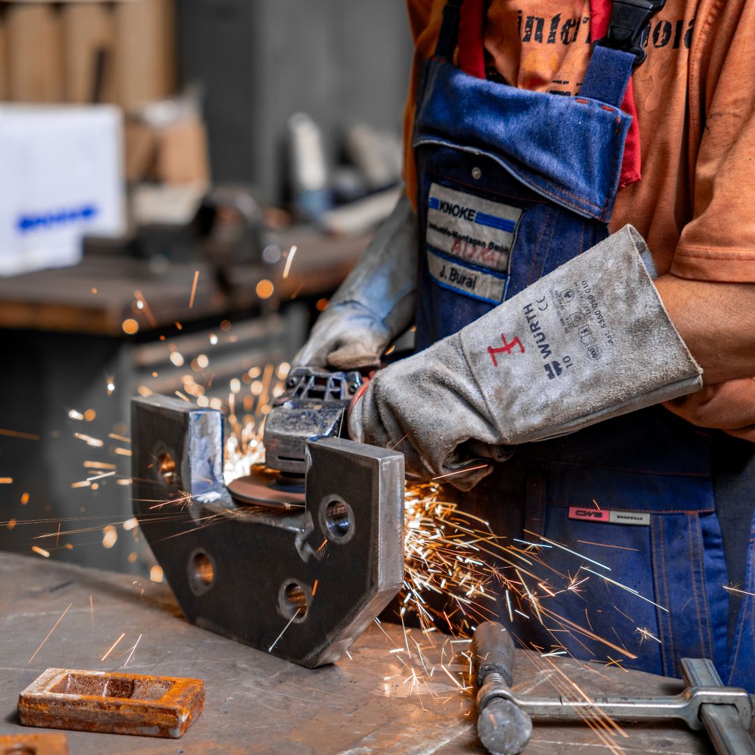 Person bei der Feinbearbeitung eines Metallteils bei dem Funken sprühen